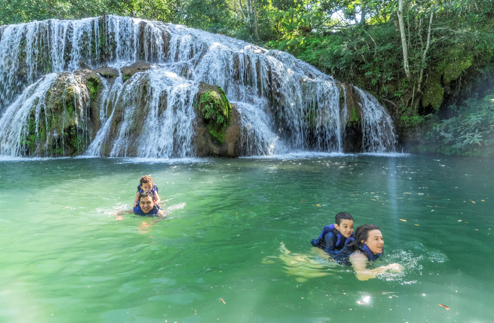 Visitantes nadam na piscina natural diante de uma cachoeira na Estância Mimosa